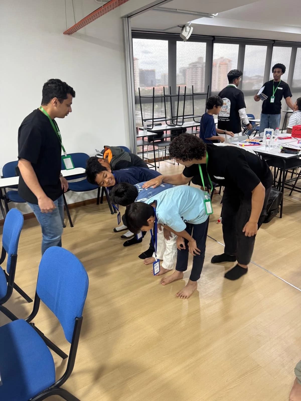 Adult mentor gently guiding a row of children practising the bowing position of prayer in a classroom.