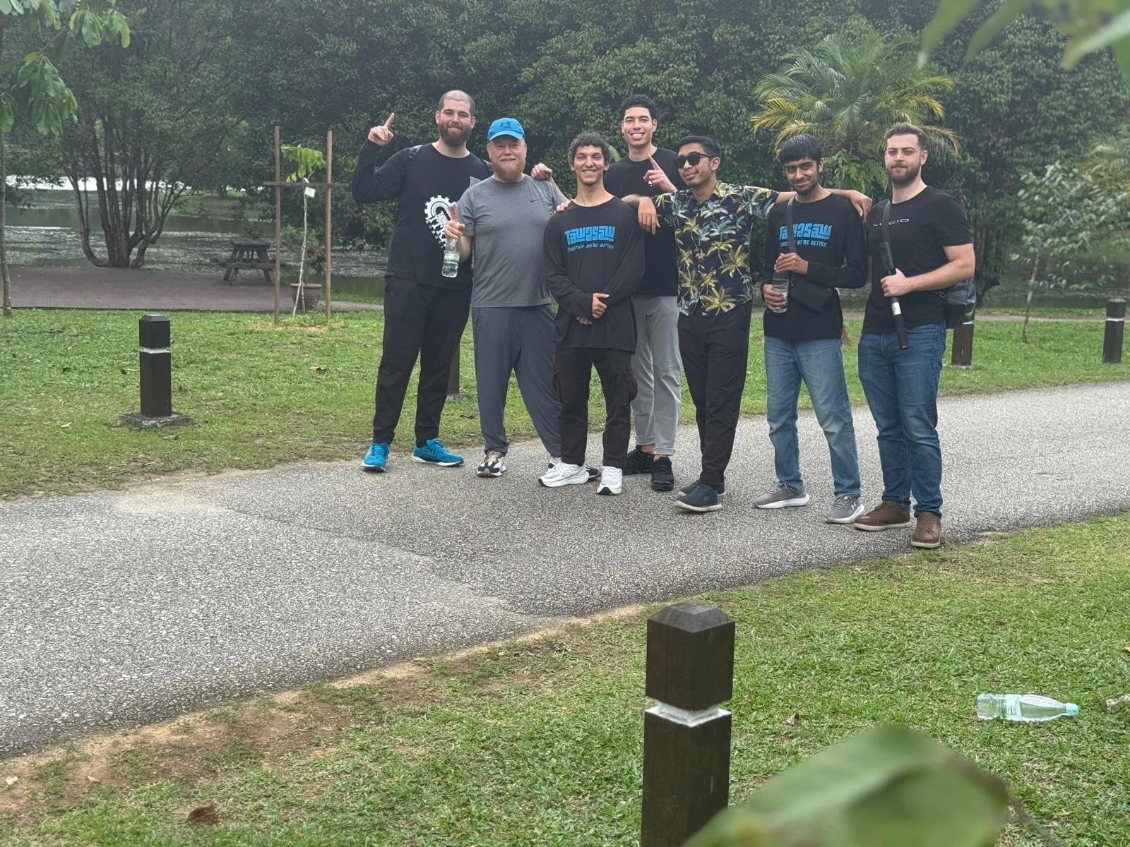 Group of young men posing on an outdoor path in a park; several wear Tawasaw 'Together We're Better' T-shirts.