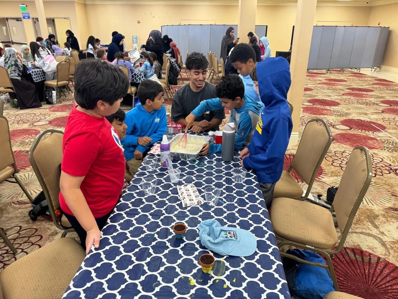Boys gathered around a young mentor whisking a dessert mixture in a foil tray.